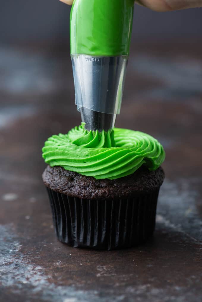 a chocolate cupcake being piped with bright green frosting