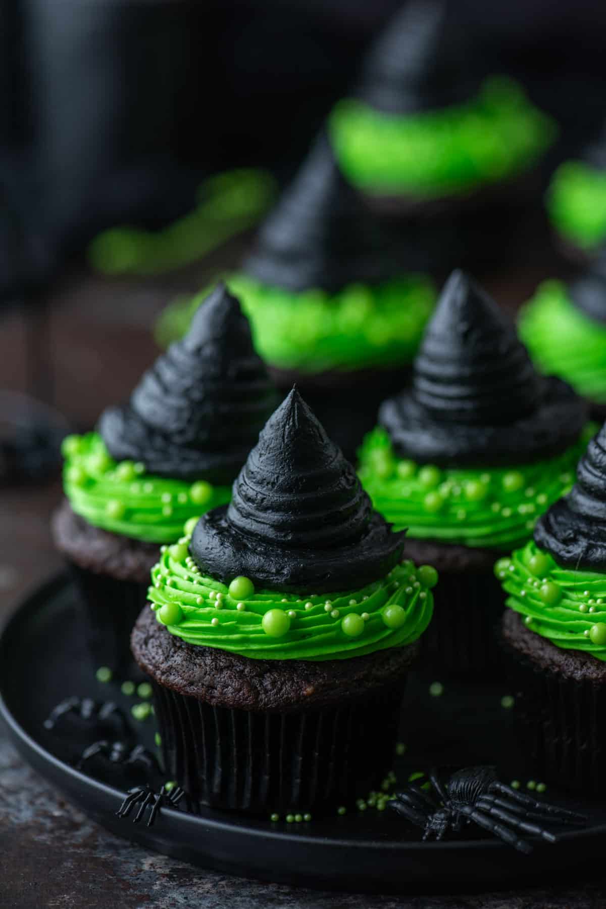 with hat cupcakes on a black plate with little black spiders scattered around