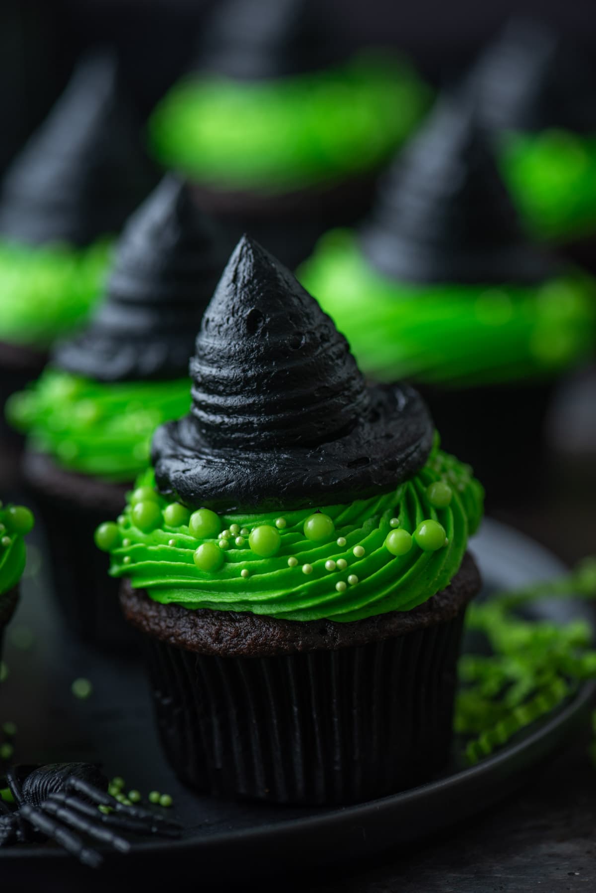 green and black witch hat cupcakes on a black plate
