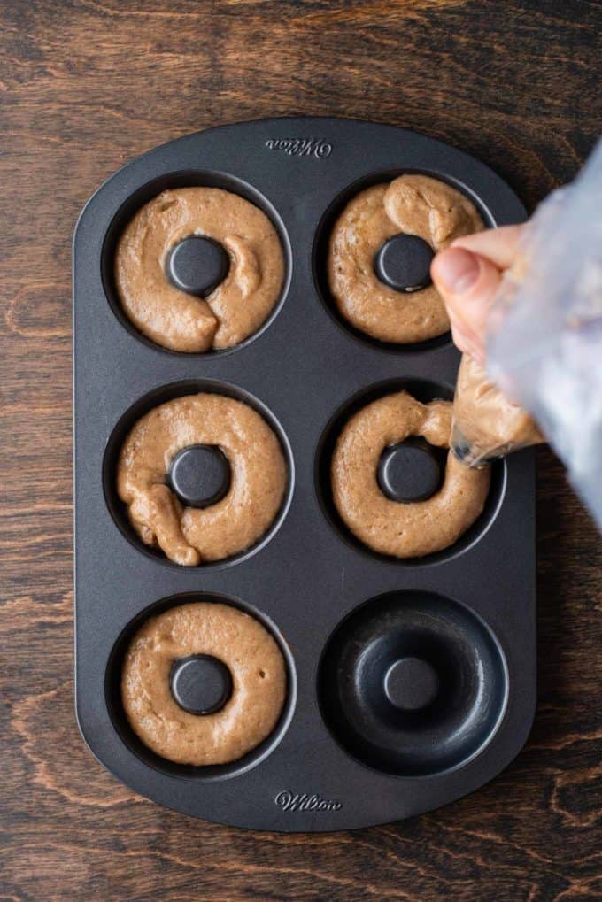 apple cider donut butter being piped into a donut pan on a wooden surface