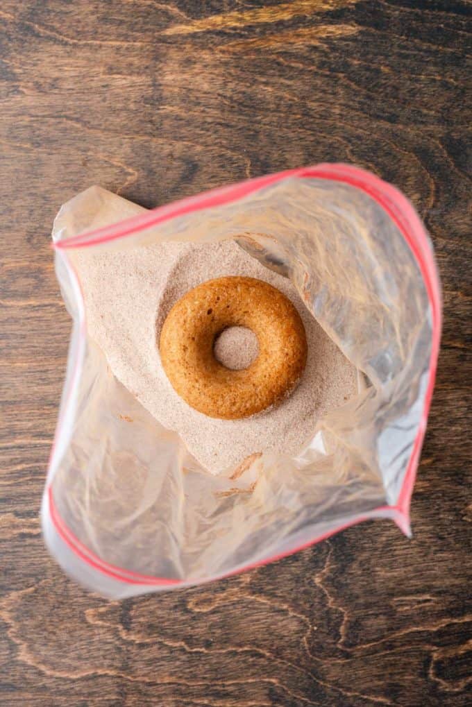 a baked apple cider donut inside a ziploc bag with a cinnamon sugar mixture in it on top of a wooden surface