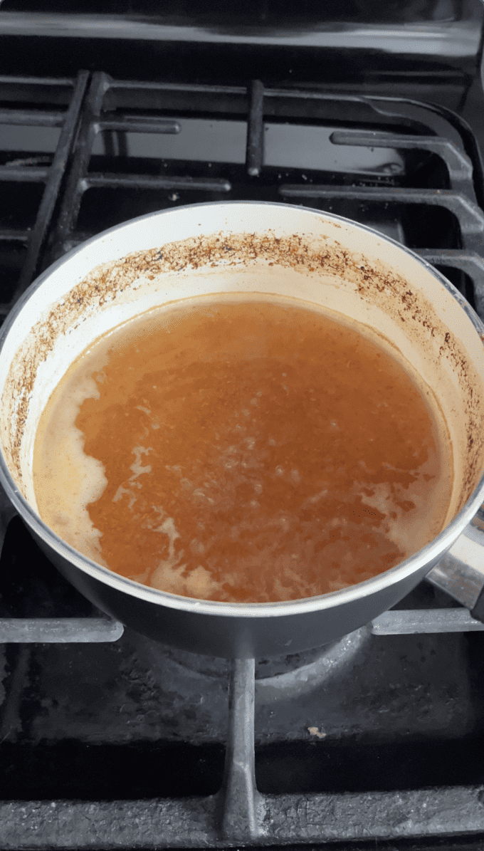apple cider reduced down in a white saucepan on an oven