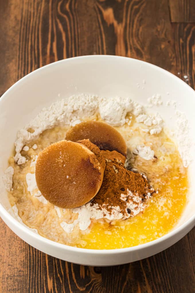 a white bowl on a wood surface with flour, brown sugar, melted butter, cinnamon and salt in it that have not been combined yet