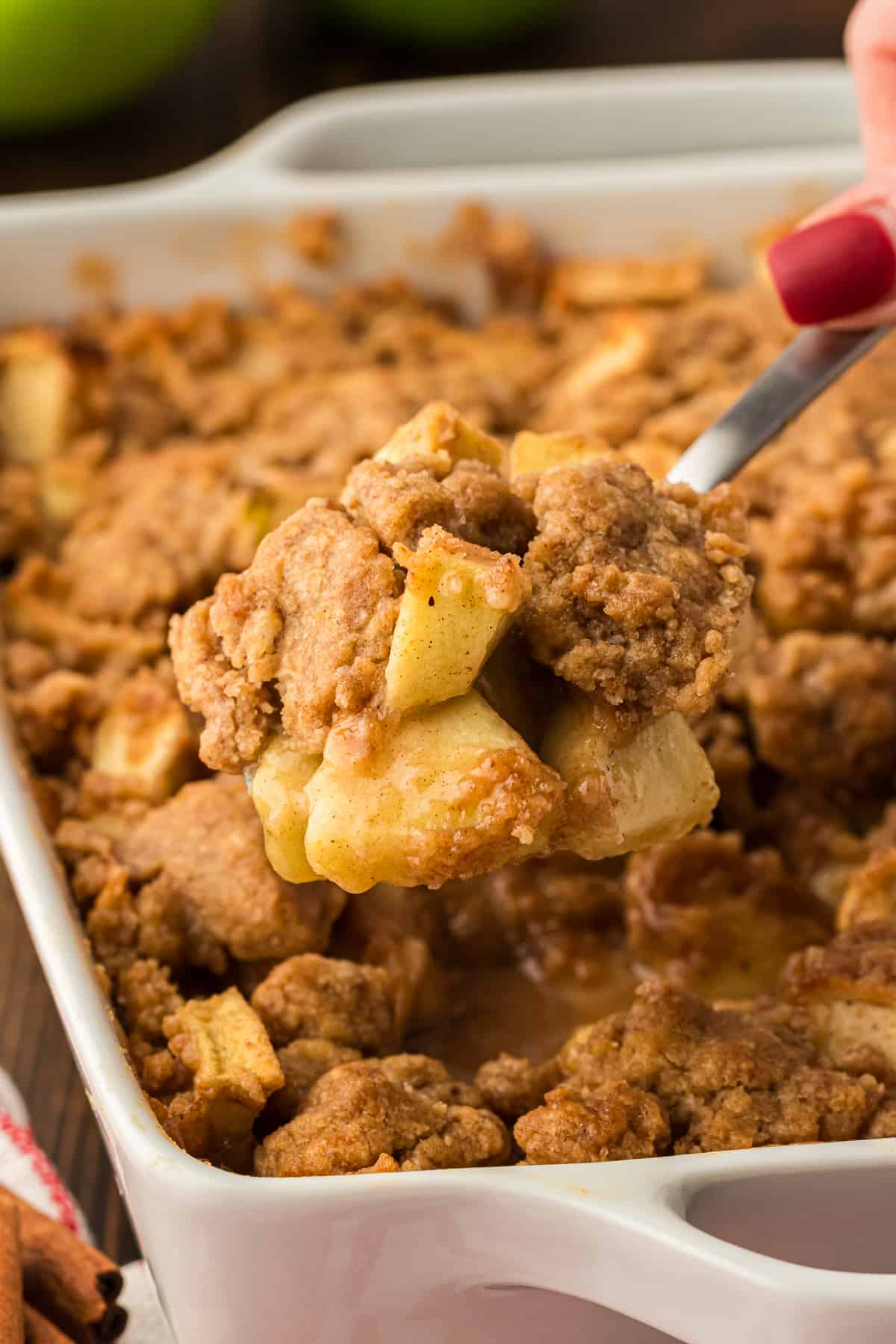 a white baking dish full of apple crumble with a spoon of apple crumble being lift above it