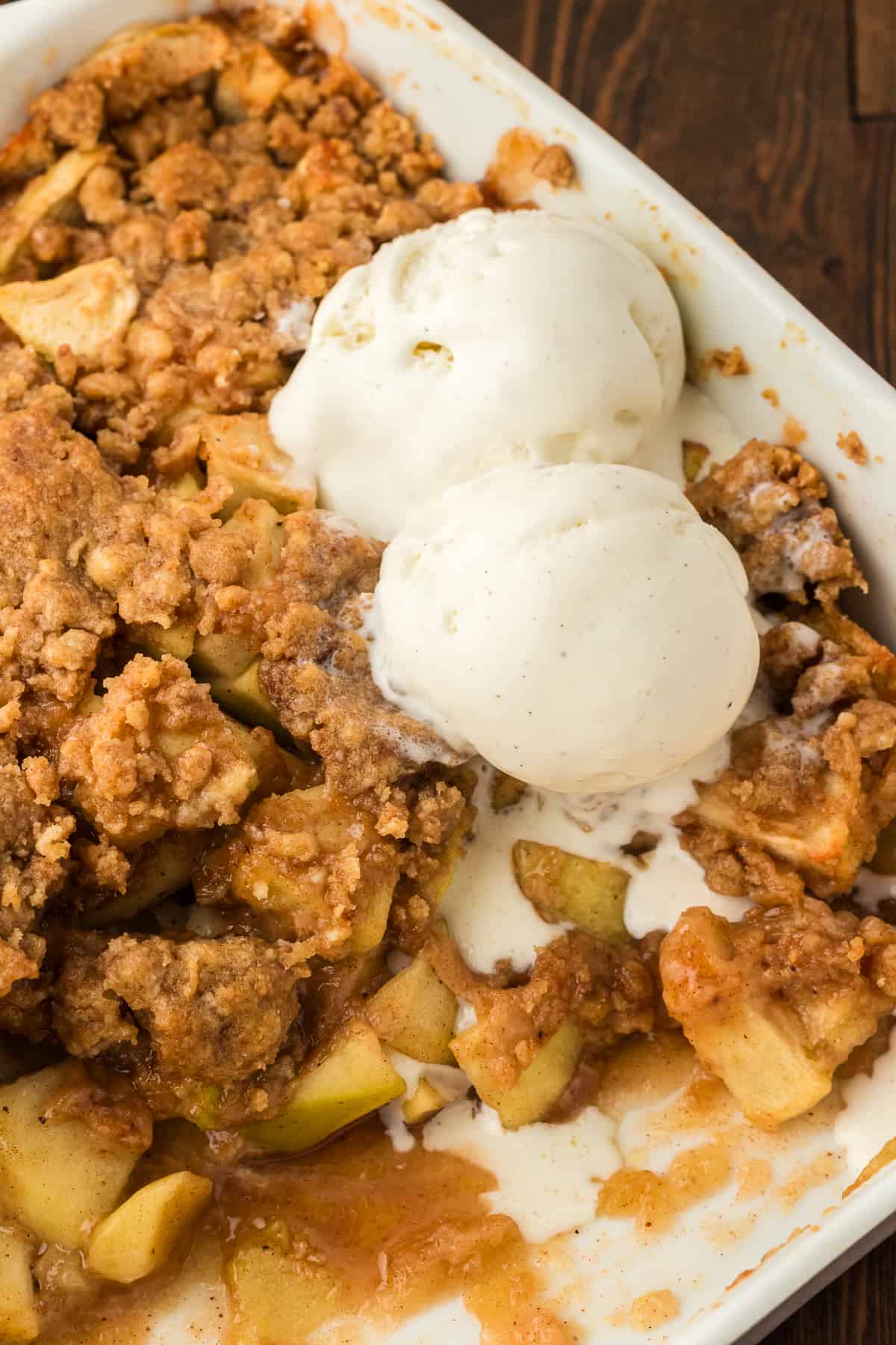 a baking dish full of apple crumble with a portion missing and two scoop of vanilla ice cream on top