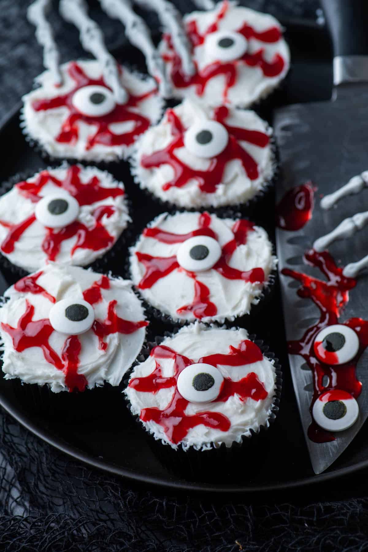 eyeball cupcakes on a black plate with a large knife and skeleton hands