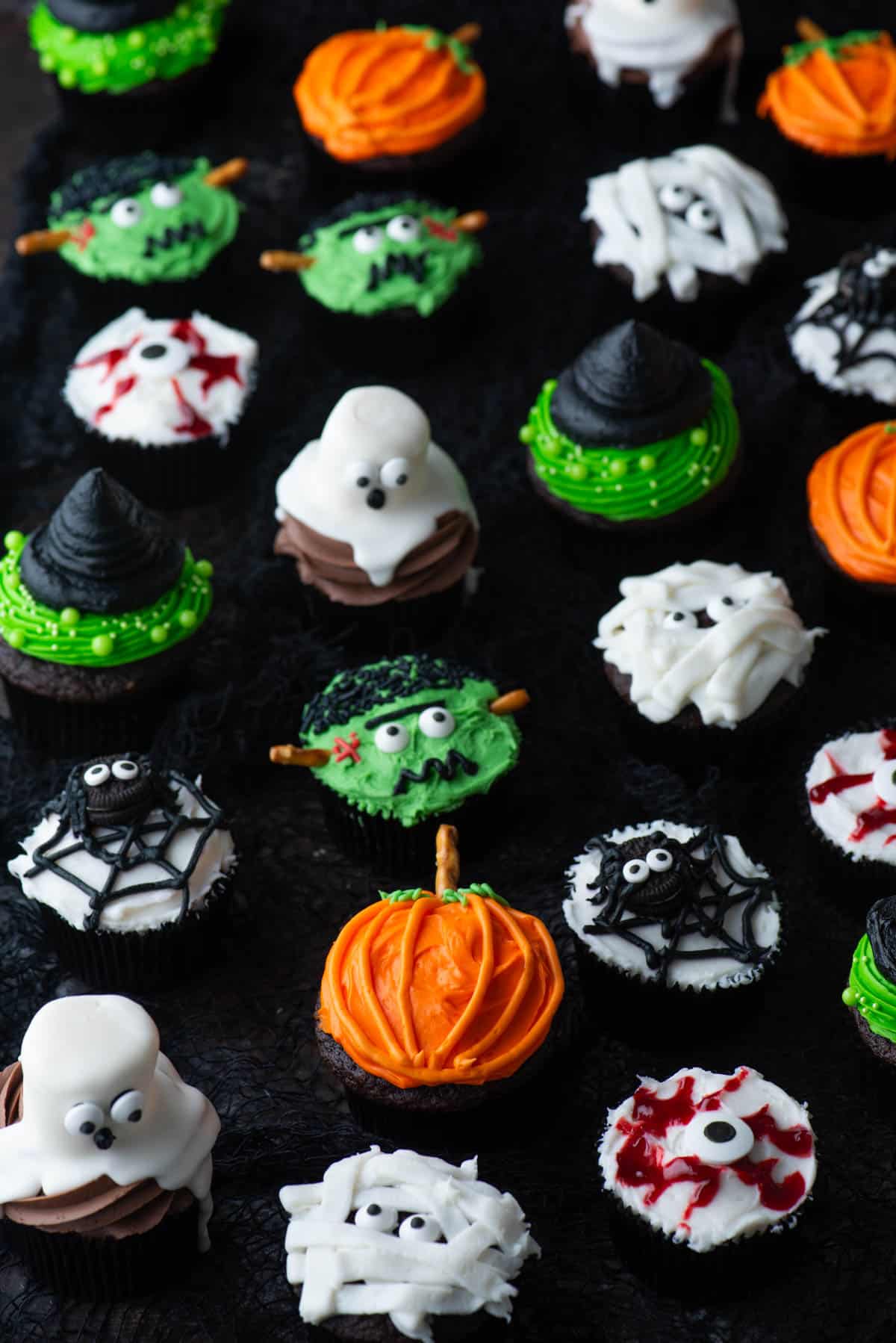 an assortment of halloween cupcakes including mummy, ghost, pumpkin, frankenstein, spider, eyeball, and witch hat pumpkins