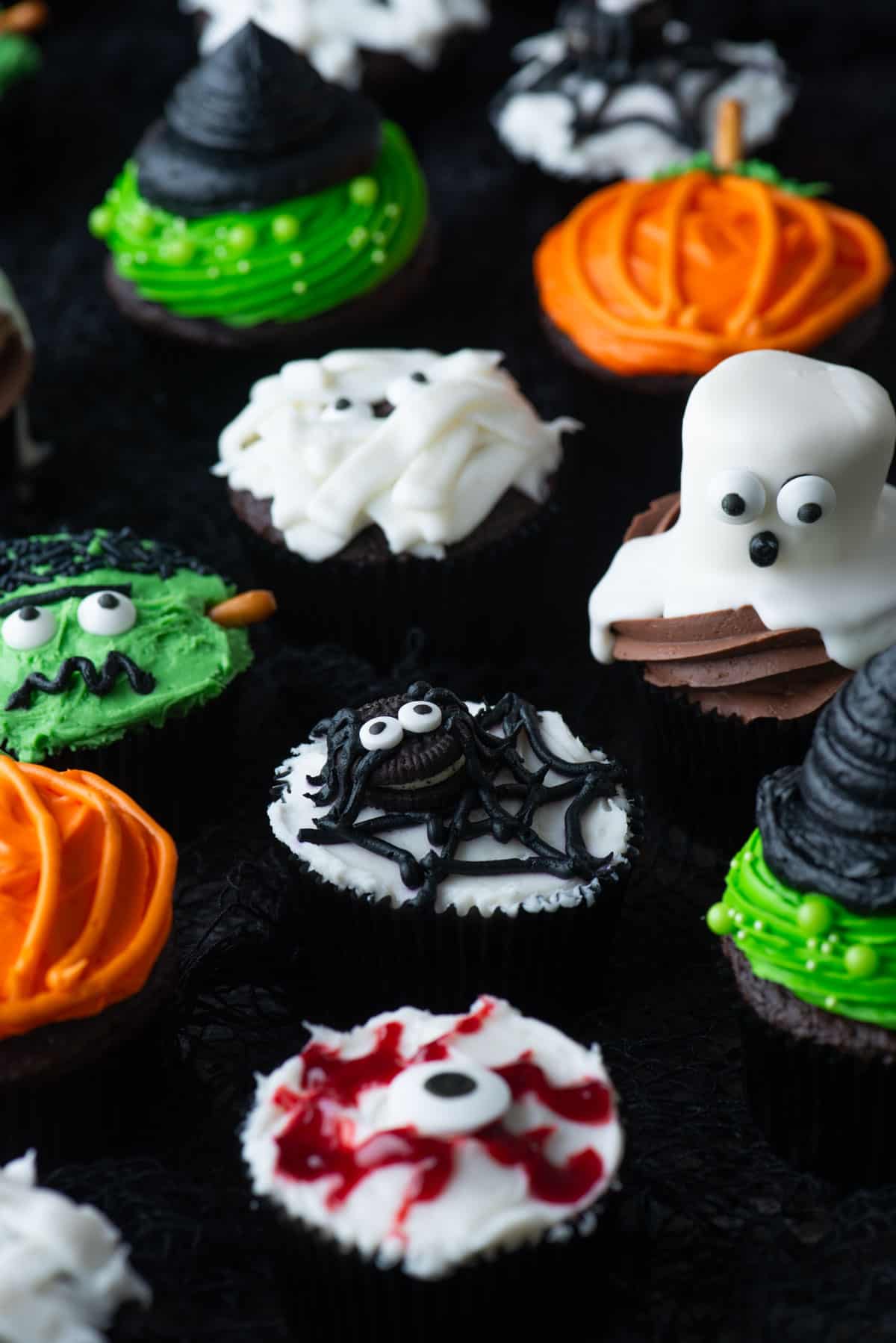 an assortment of halloween cupcakes including mummy, ghost, pumpkin, frankenstein, spider, eyeball, and witch hat pumpkins