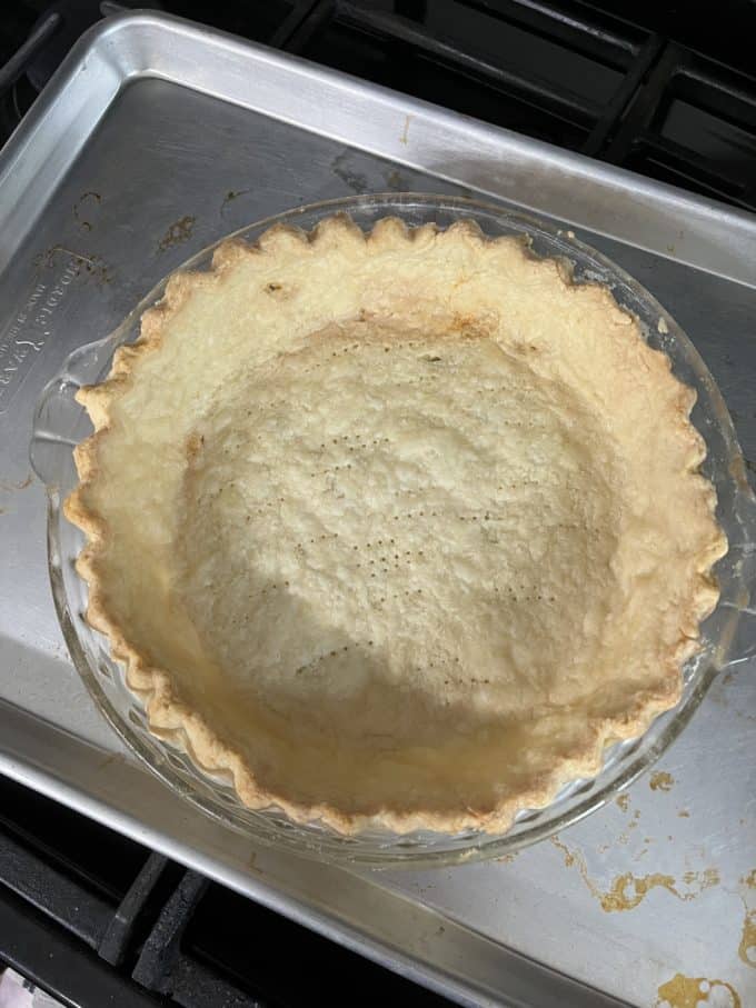 pie crust baking in a clear glass pie dish on top of a silver baking tray