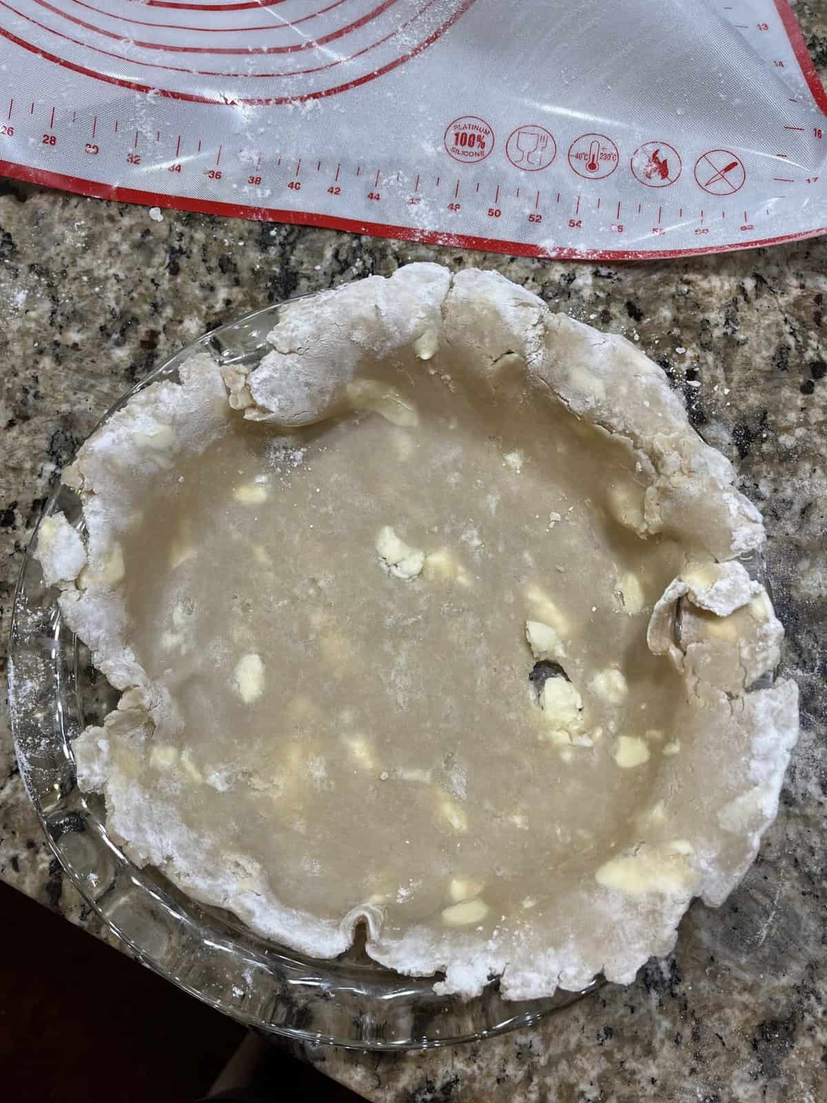 pie crust unfinished in a glass pie dish on a granite countertop beside a pie mat