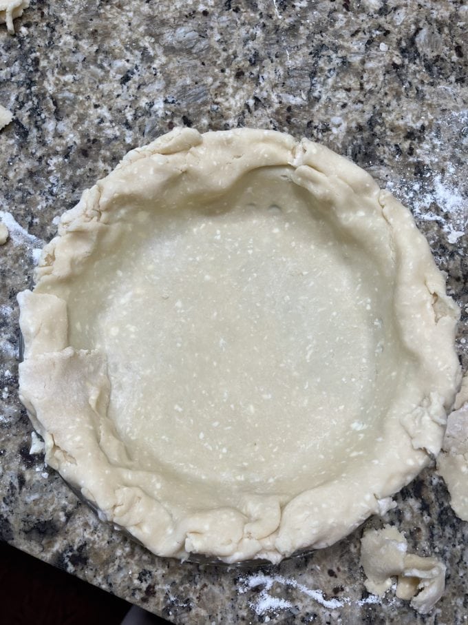 pie crust in a pie pan on a granite counter top with some flour sprinkled around