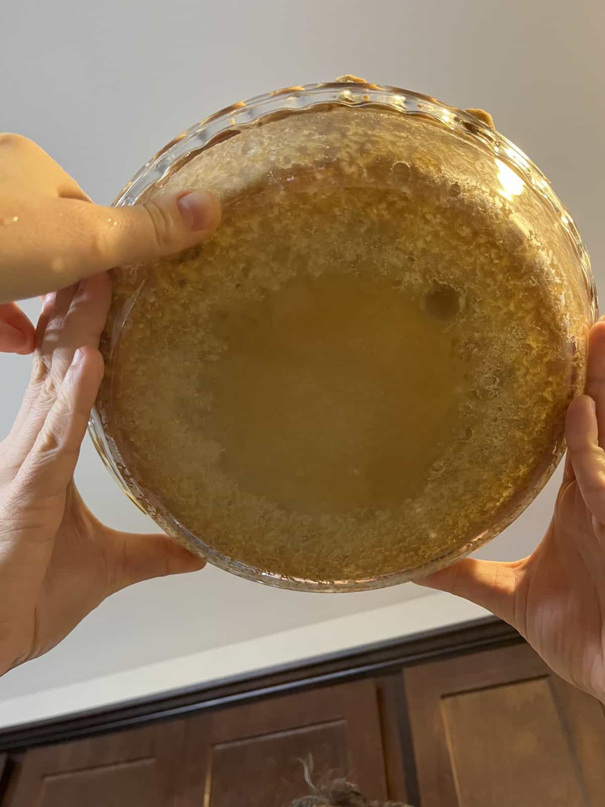 three hands holding up a pie crust in a clear glass pie dish showing it from underneath