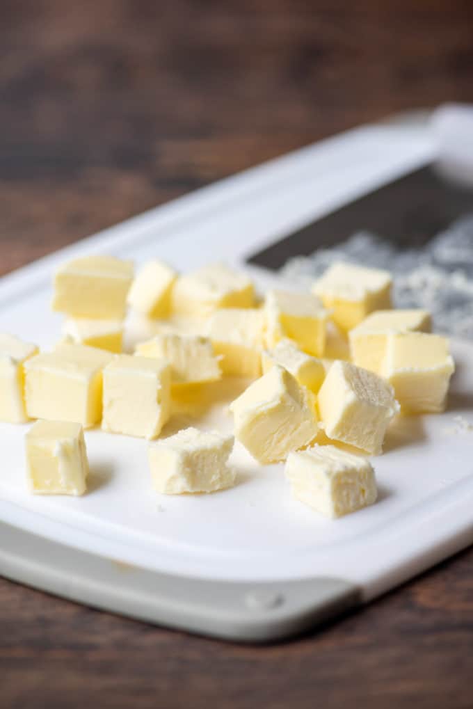 cubes of butter and a pastry cutter on a white cutting board on a wood surface