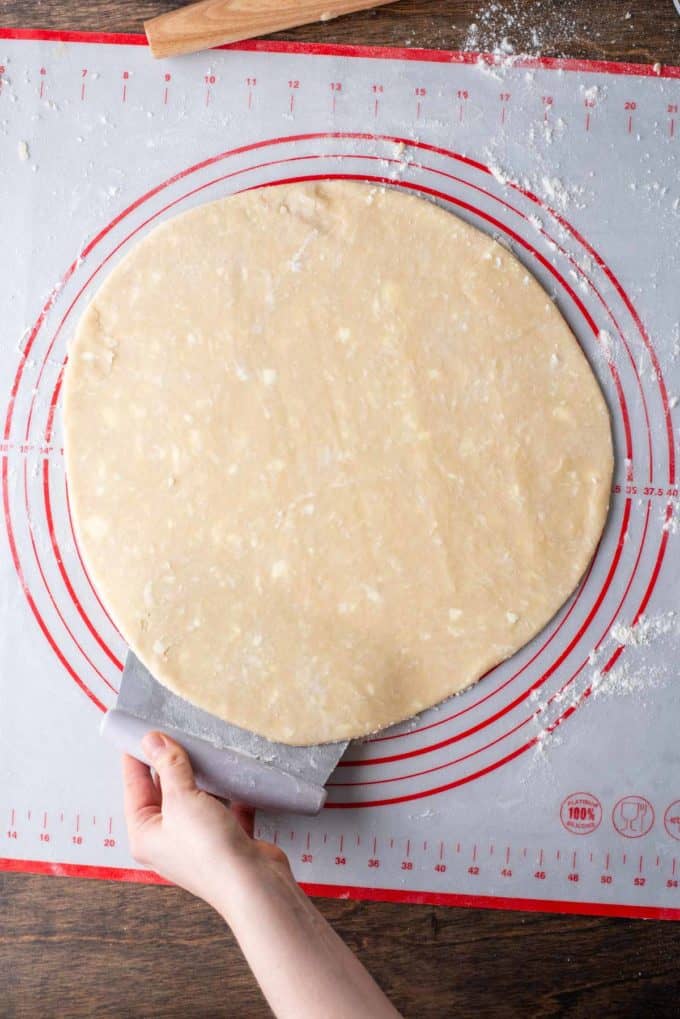 pie crust dough being slightly lifted on one side by a pastry cutter from the red and white pie mat its sitting on