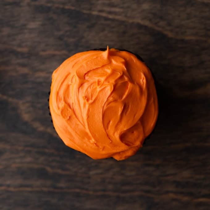 a cupcake with orange frosting on it on a wood surface