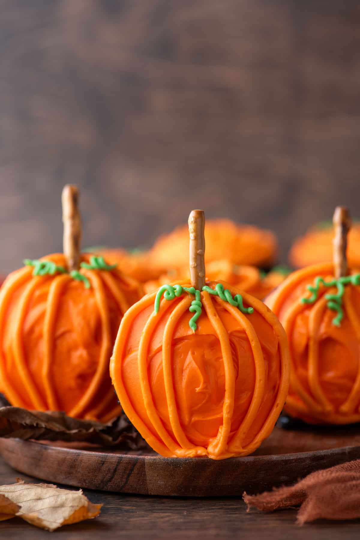 pumpkin patch cupcakes on a wood plate standing up on their sides so the pretzel stick stems are standing up straight