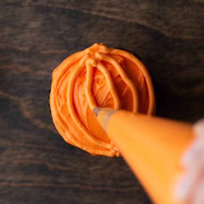a cupcake with orange frosting on a wood surface with orange lines being piped on it