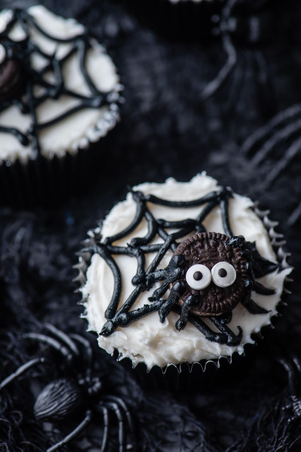 a spider web cupcake on top of black netting with black plastic spiders around it and another cupcake in the background