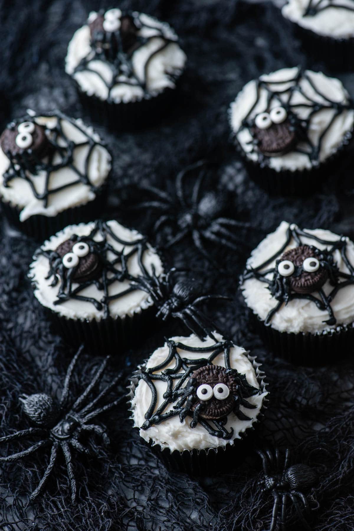 spider web cupcakes arranged on a black netting with black plastic spiders around them