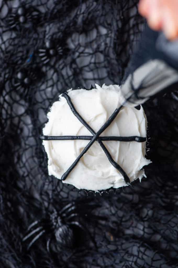 piping black lines on a cupcake to make a spider web decoration