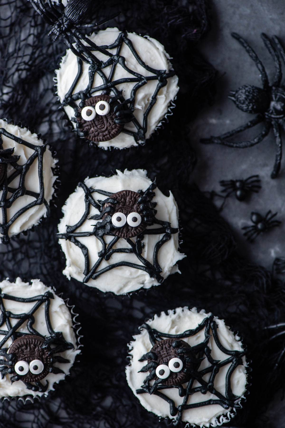 spider web cupcakes arranged on top of a black netting with mini plastic black spiders around them