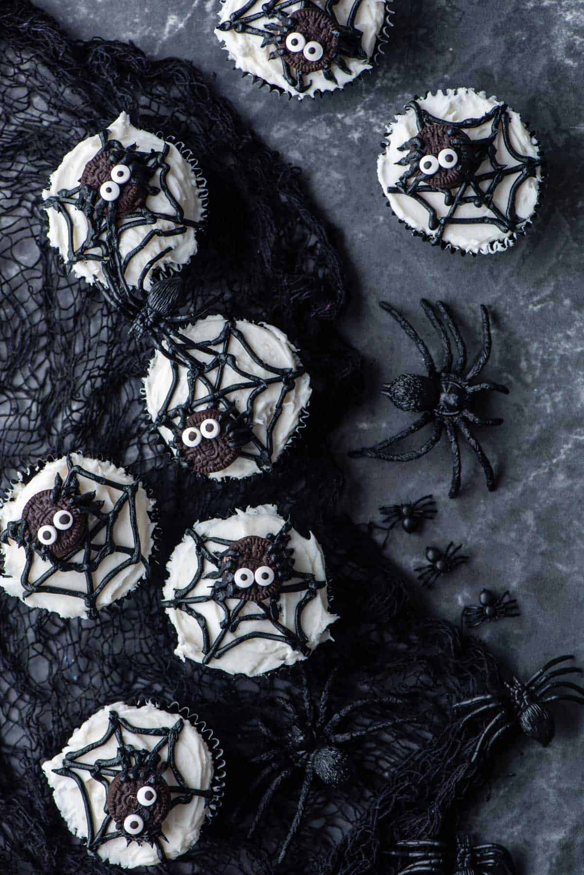 spider web cupcakes arranged on and around a black netting with plastic spiders scattered around