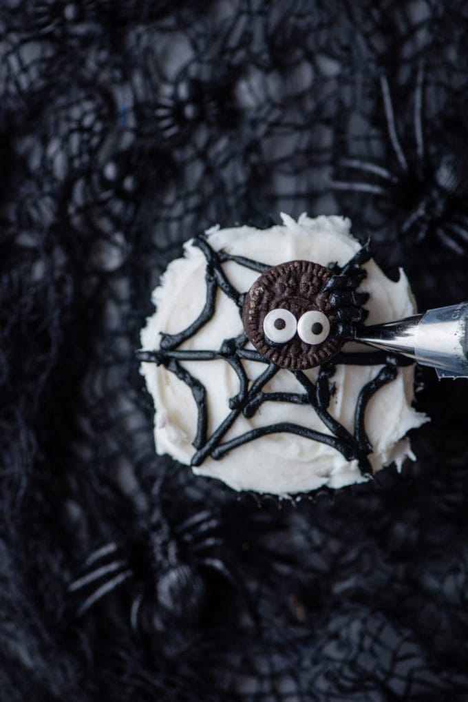 piping legs onto a mini oreo to make a spider on a spider web cupcake