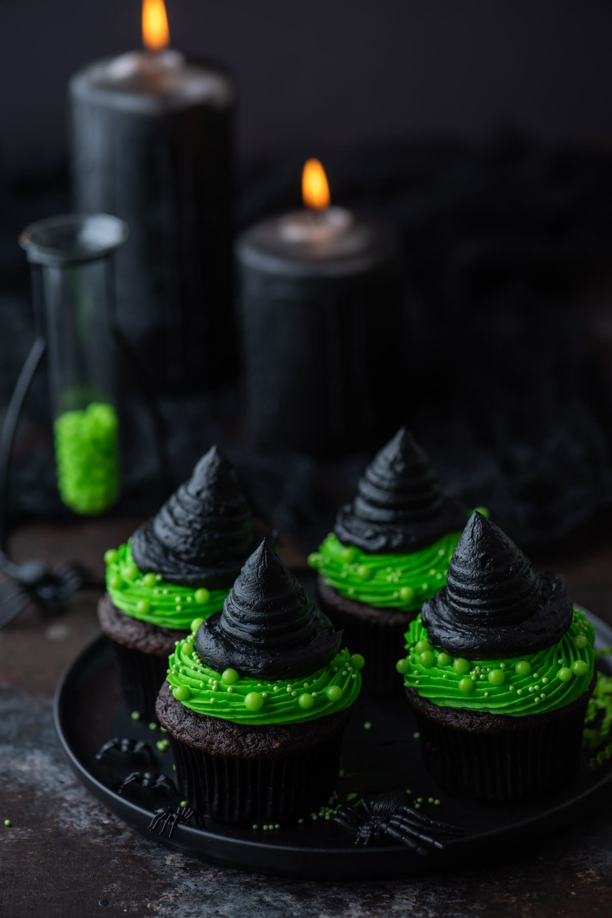 Witch hat cupcakes on a black plate with black candles in the background
