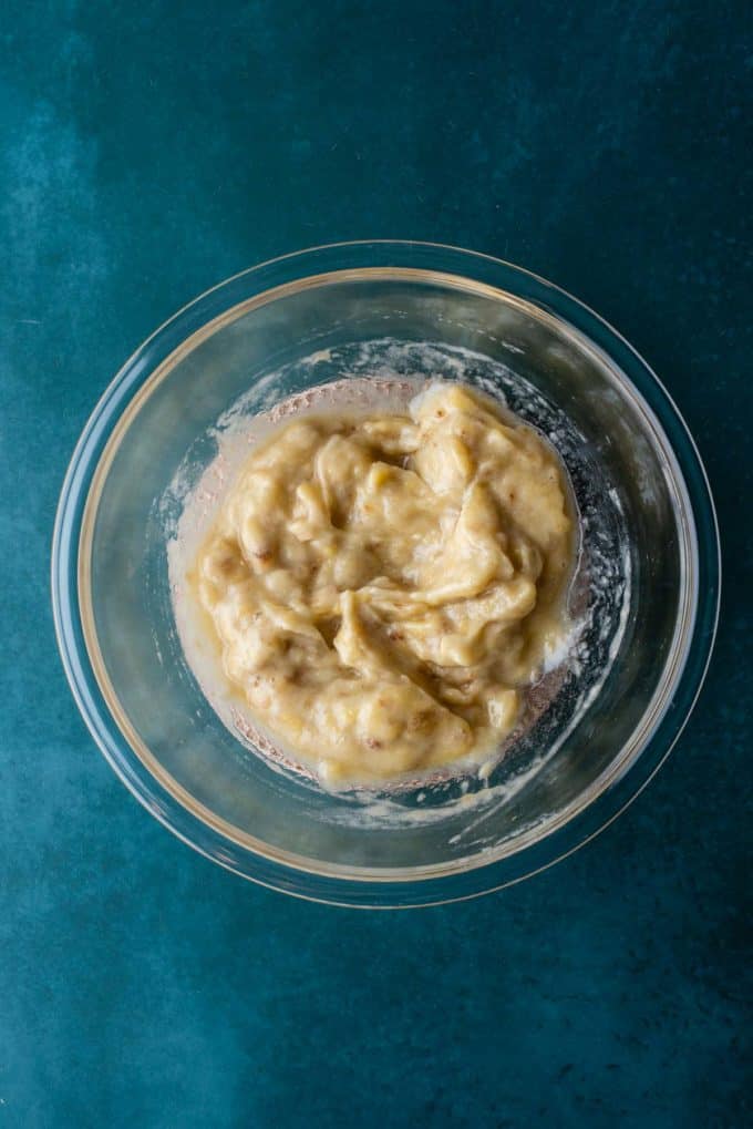 mashed bananas in a clear glass bowl on a dark teal surface