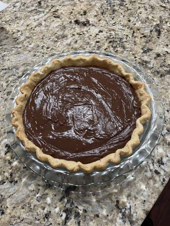 a chocolate pie ready to bake in a glass pie dish sitting on top of a granite kitchen counter