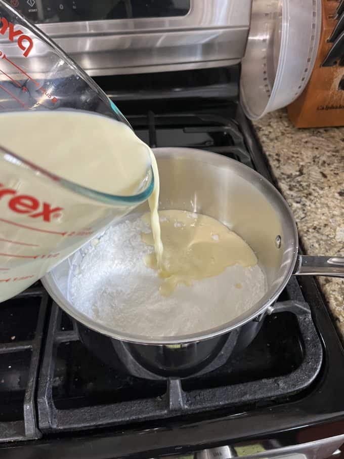 a combination of egg yolks and milk being poured over a mixture of cornstarch, sugar and salt in a pot on top of an stove