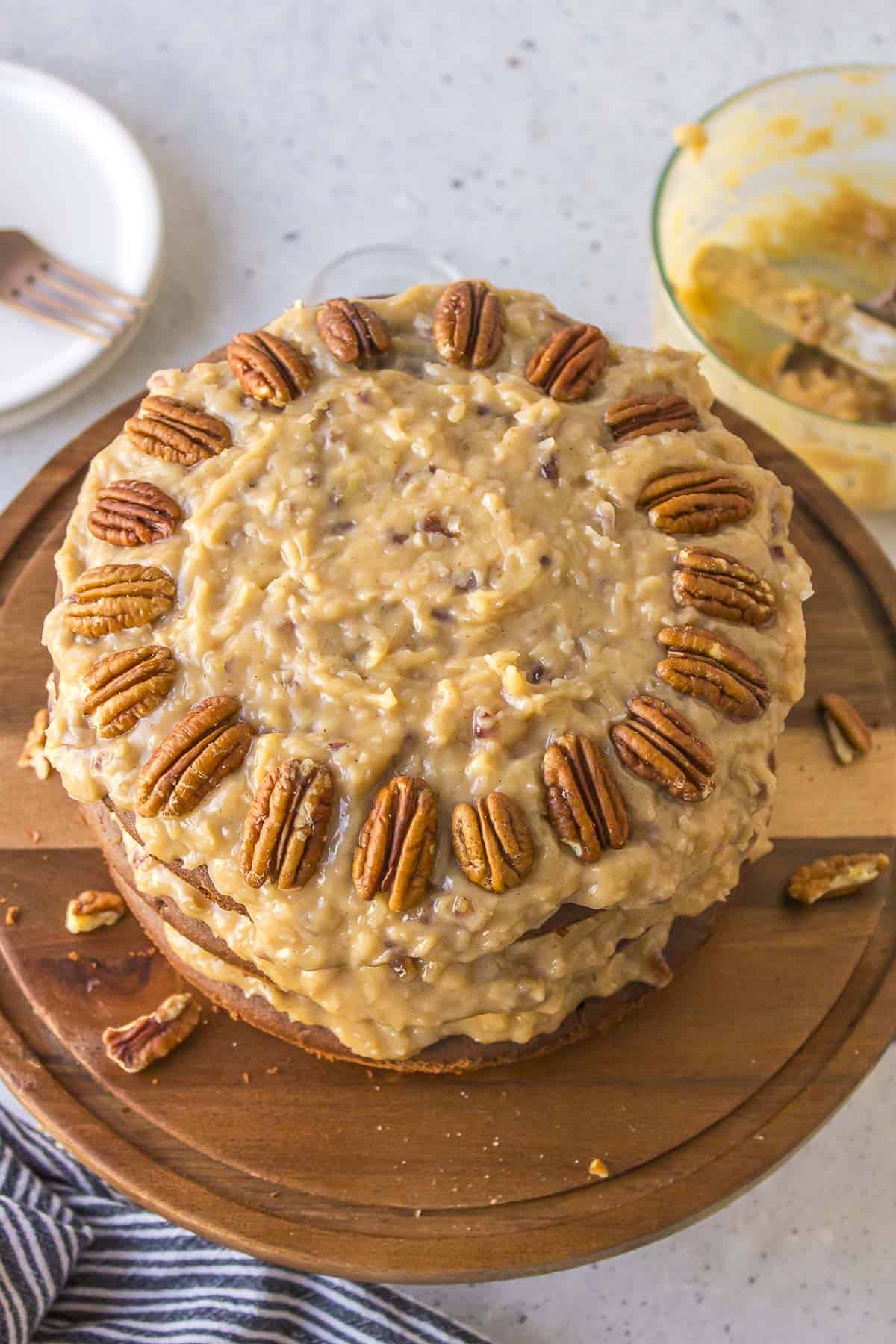 the top view of a german chocolate cake topped with coconut pecan frosting and a ring of whole pecans on a wood cake platter