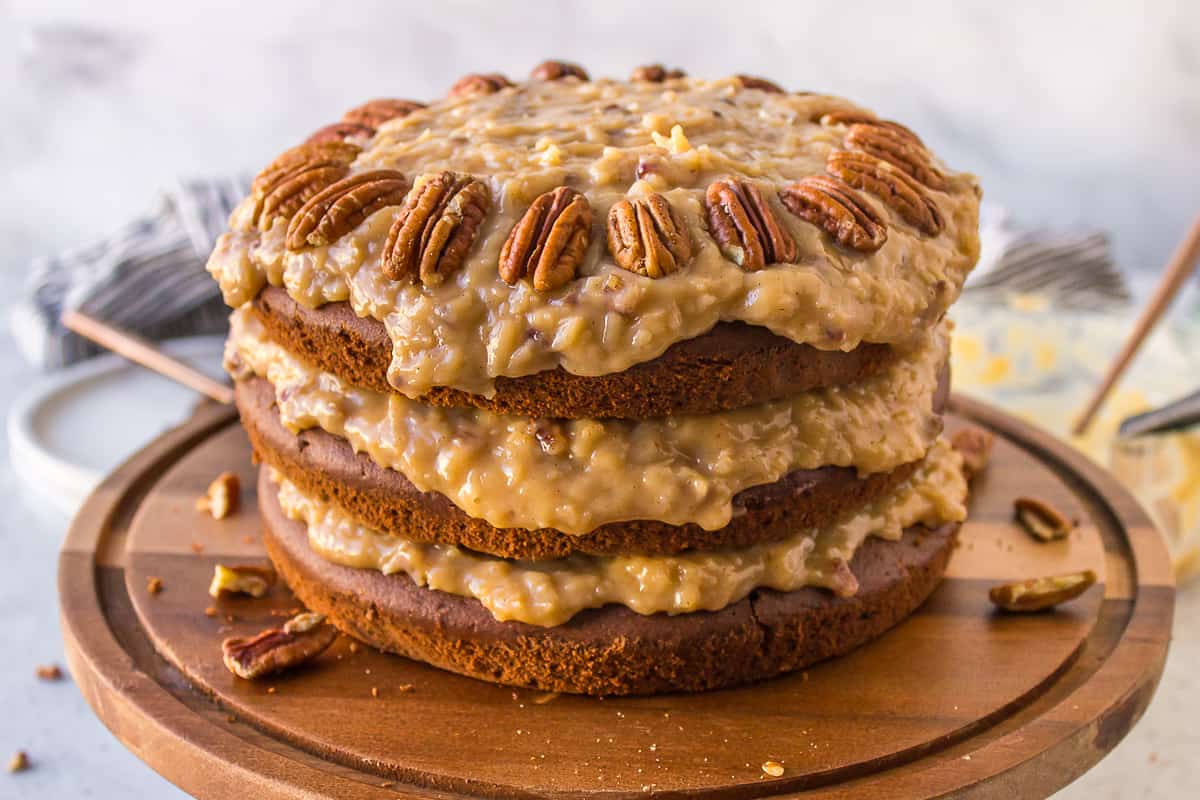 German chocolate cake on a wood serving platter with pecans sprinkled around it
