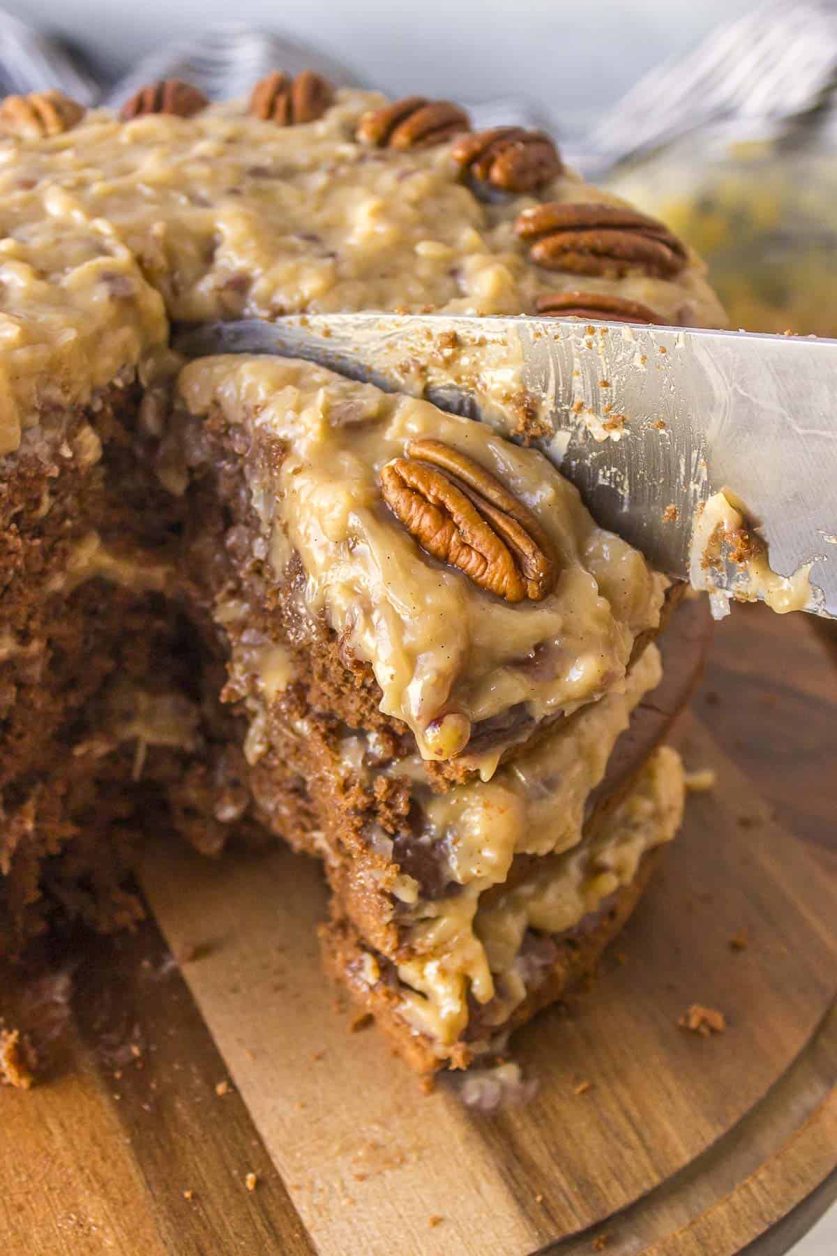 close up of a german chocolate cake on a wood serving platter being sliced