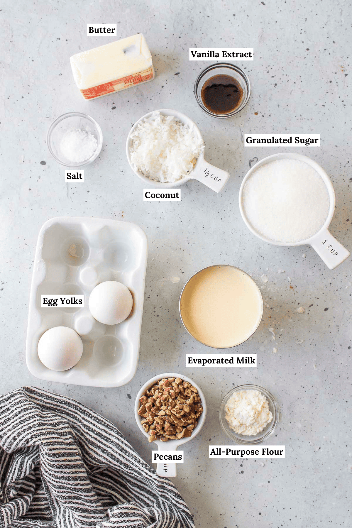 ingredients for german chocolate cake frosting including butter, vanilla extract, salt, coconut, granulated sugar, egg yolks, evaporated milk, pecans, and all-purpose flour