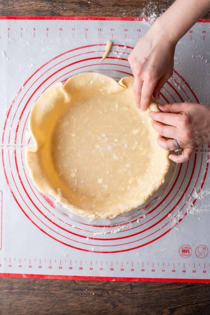 pie crust edges being folded over a pie dish that is sitting on top of a red and white pie mat