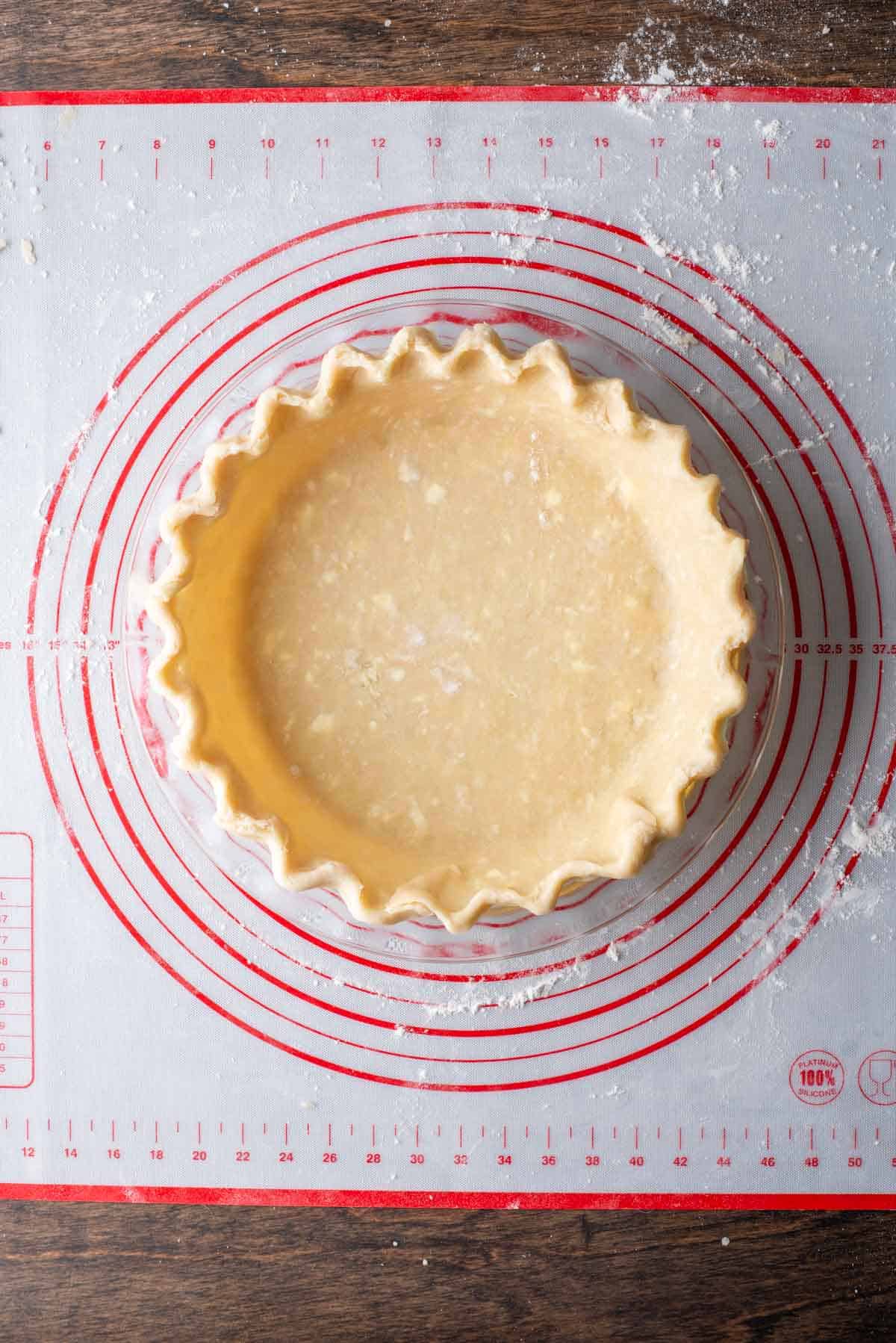 pie crust in a pie pan on top of a red and white pie mat with flour sprinkled around