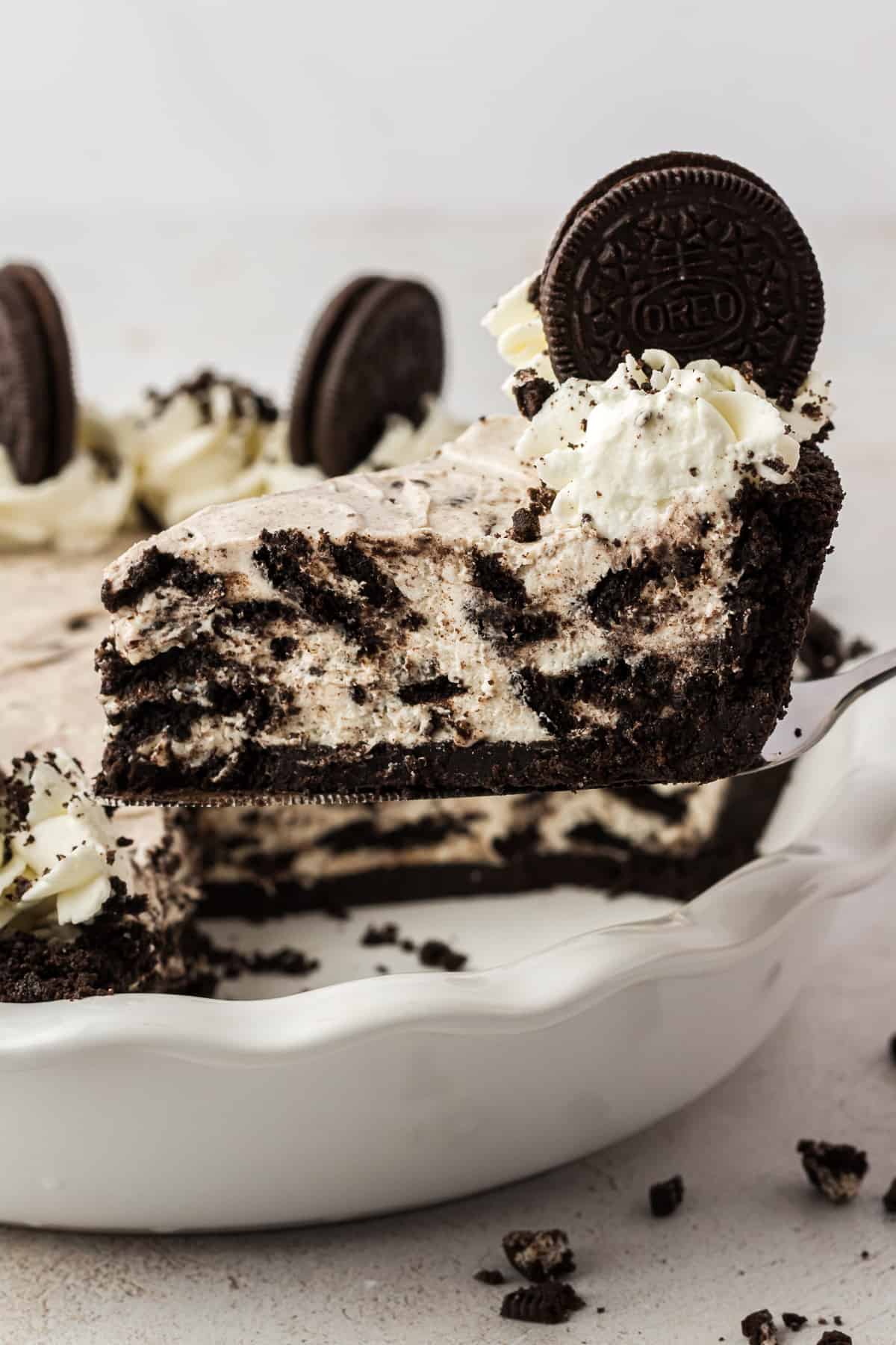 a piece of oreo pie being lifted out of a white pie dish full of oreo pie