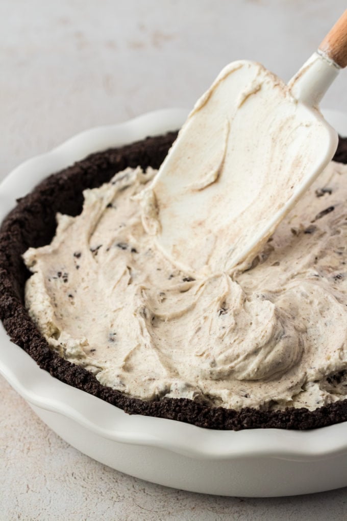 oreo pie filling being spread with a spatula into an oreo pie crust in a white pie dish