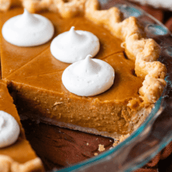 pumpkin pie in a glass pie dish topped with dollops of whipped cream