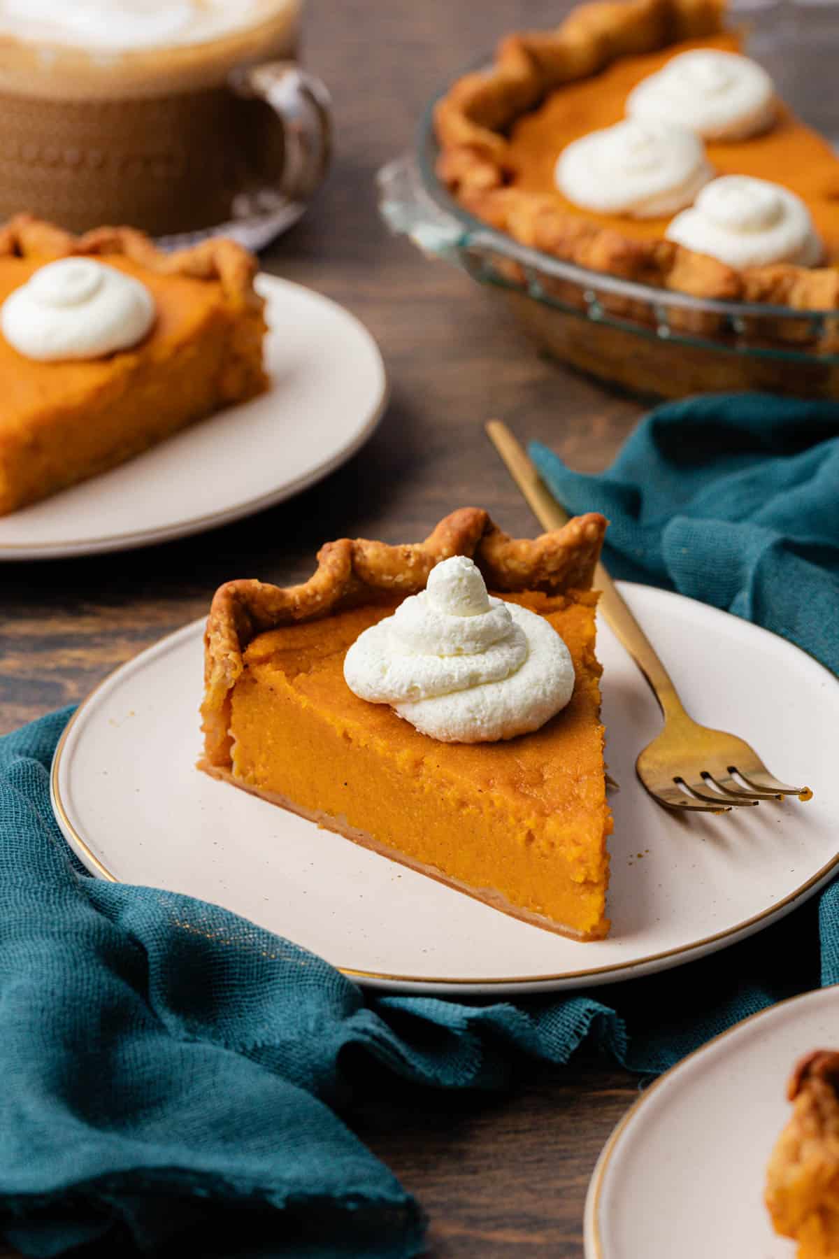 slices of sweet potato pie on white plates topped with dollops of whipped cream, with a fork sitting beside the pie on the front plate and a dark teal towel underneath the plate