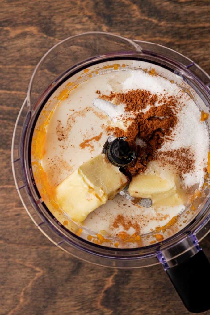 mashed sweet potato, milk, sugar, cinnamon, nutmeg and butter in a food processor bowl sitting on a wood surface
