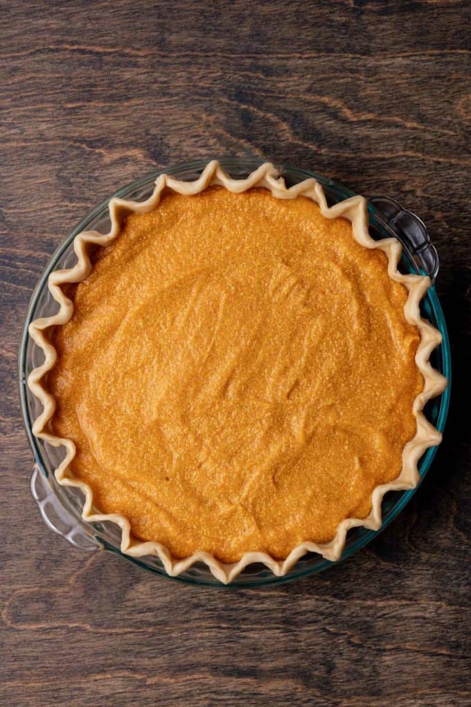 sweet potato pie ready to be baked in a glass pie dish sitting on a wood surface