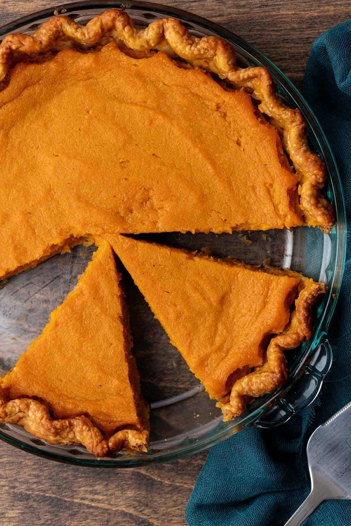 sweet potato pie in a glass pie dish with half of it unsliced and the other half with slices missing sitting on a wood surface