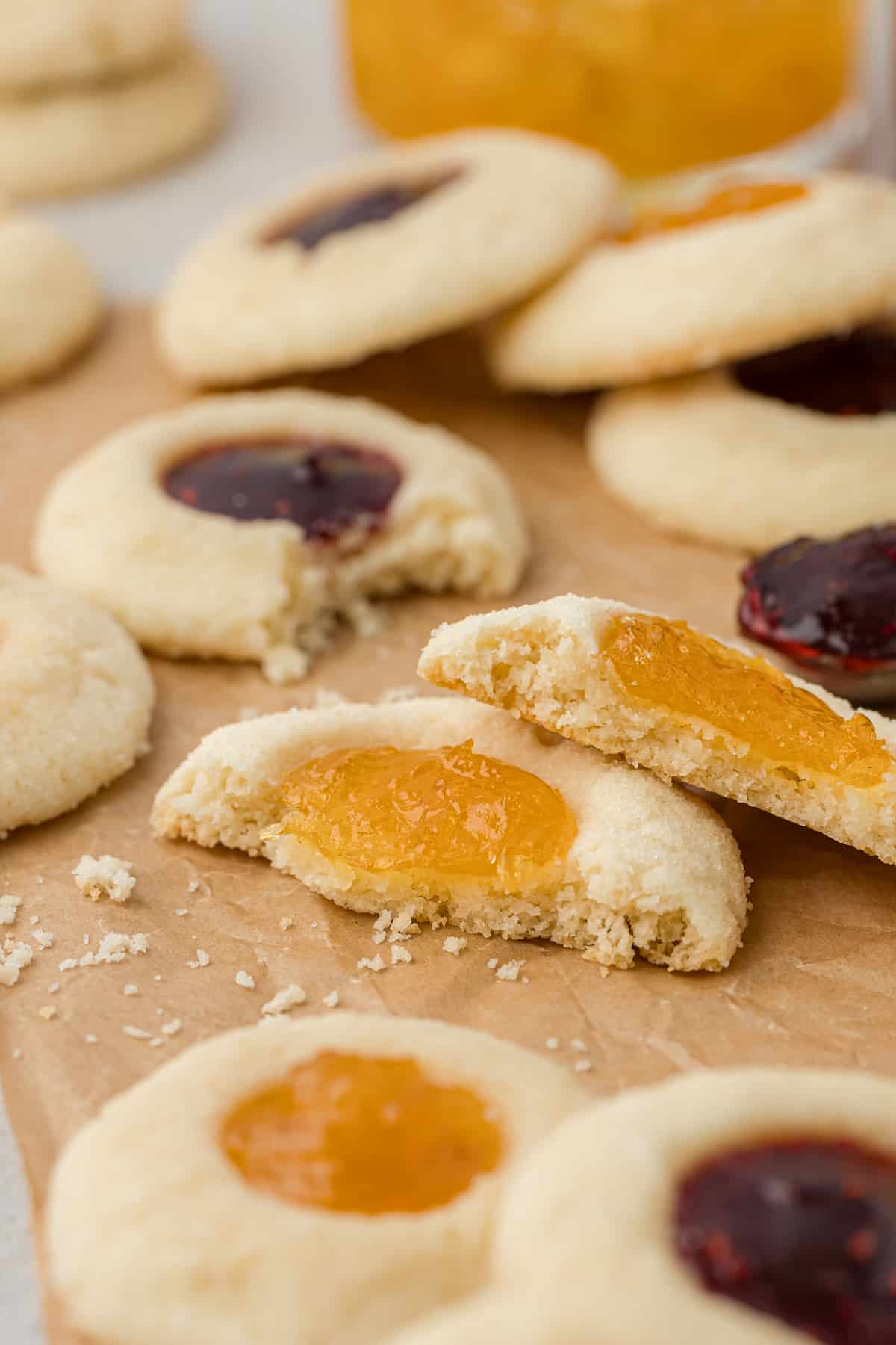 close up of thumbprint cookies on brown paper, some half eaten or broken in half with more whole cookies scattered around