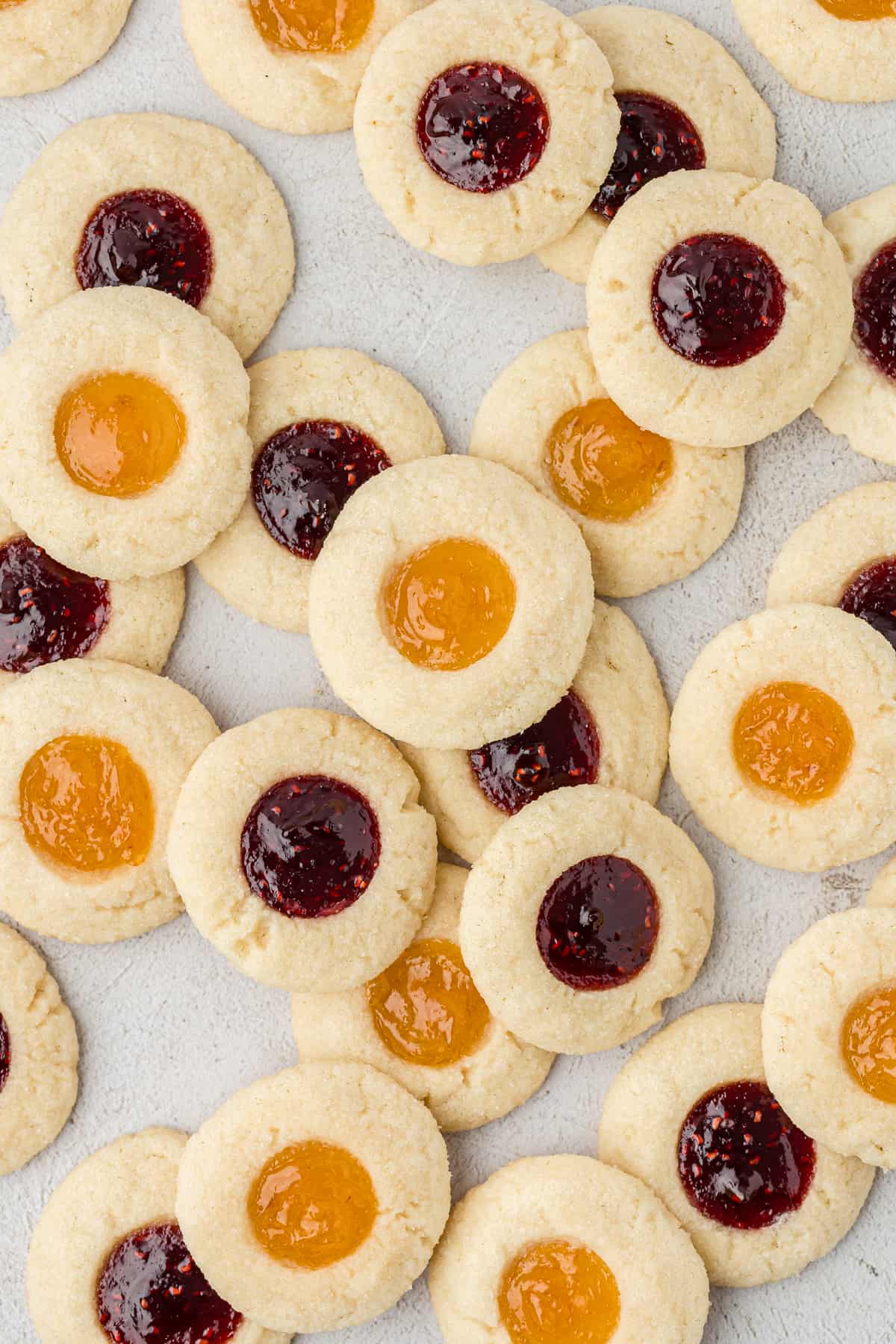 an assortment of thumbprint cookies stacked and scattered around each other on a countertop surface