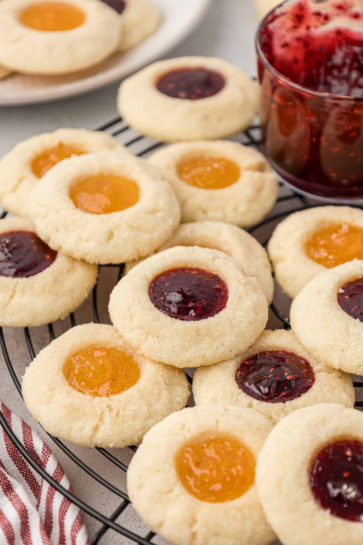 apricot and raspberry jam thumbprint cookies scattered on a wire rack beside a jar of raspberry jam