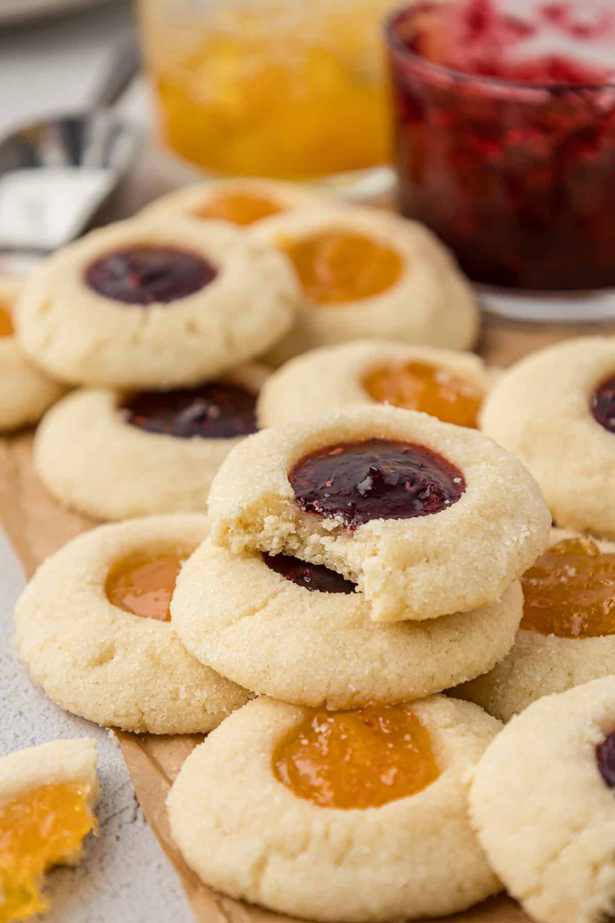 an assortment of raspberry and apricot jam thumbprint cookies with jars of jam in the background