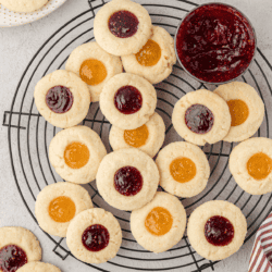 an assortment of thumbprint cookies on a wire rack with a bowl of raspberry jam
