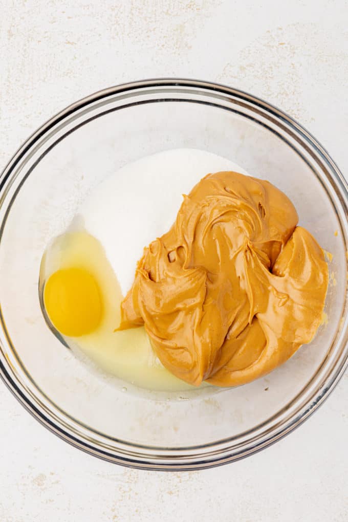 one egg, sugar and peanut butter in a clear glass bowl